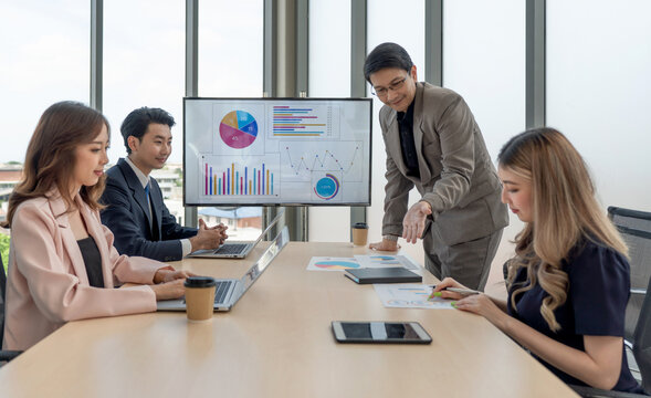 Group of business people are gathered in a meeting room, discussing and sharing ideas around a large conference table.
