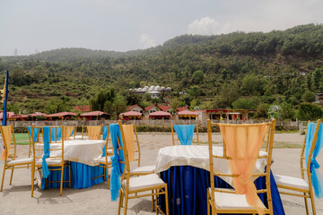 Festive outdoor dining setup with decorated tables and chairs against a scenic mountain backdrop,...