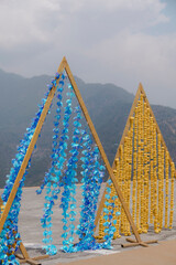 Blue and yellow triangular flower garlands decorate an outdoor venue with a mountain backdrop,...