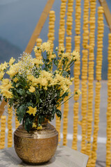 Floral centerpiece with yellow flowers in a brass vase, set against a backdrop of yellow floral...