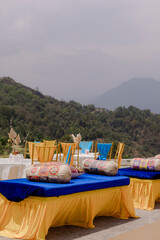Outdoor event setup with cushioned seating and mountain backdrop. Tables and chairs set for dining against a lush landscape.