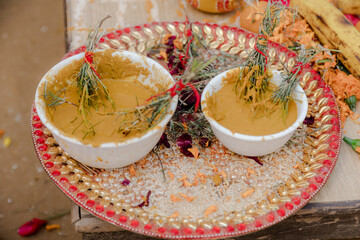 Traditional Haldi Ceremony Items: Two bowls filled with a yellow paste and tied herbs are placed on...