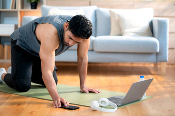 Young asian man doing plank exercise in living room at home while watching online workout tutorial...
