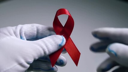 White Glove Hand Displaying a Red Ribbon on a White Background Representing HIV and AIDS Awareness Symbolizing Support and Hope - Powered by Adobe