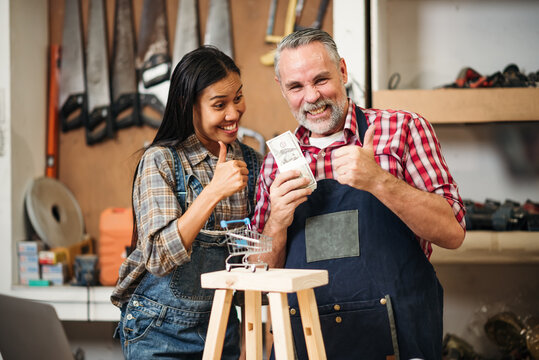 Senior Carpenter and Asian Woman Using Laptop to Sell Handmade Woodwork Products on E-commerce Platform in Craft Workshop