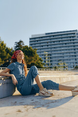 Fototapeta premium Lifestyle woman in modern boho-western denim street style relaxing outdoors under warm sunlight with a film color aesthetic and casual sneakers.