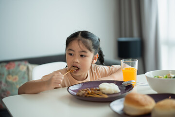 Young girl enjoying meal at home, sitting at table with various dishes, focused on food, bright...