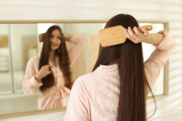 Fototapeta premium Smiling teenage girl brushing her shiny hair near mirror at home, selective focus