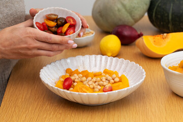 A person prepares a vibrant vegan salad with roasted pumpkin, tomatoes and chickpeas