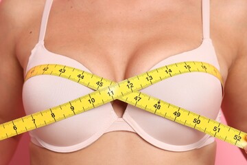 Woman in beautiful bra measuring breast circumference on pink background, closeup