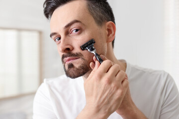 Handsome man shaving with razor at home, closeup