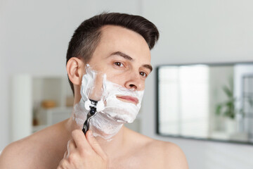 Handsome man shaving with razor at home