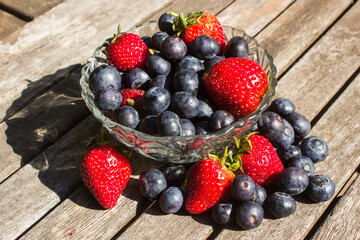 A glass bowl, filled to overflowing with bright red strawberries and indigo-colored blueberries on...