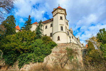 Fototapeta premium Historic medieval castle on rocky hill with lush trees and blue sky