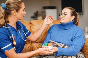 Caregiver providing medication guidance to a senior woman at home during a cozy indoor setting in...