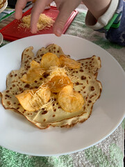 Child’s hand prepares unique snack: pancake topped with grated cheese and potato chips, image...