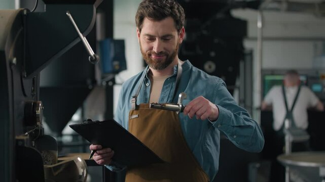 Caucasian man check coffee roasted aroma beans roaster machine equipment expert technologist inspect industry fresh caffeine roasting male guy writing notes checking quality go away control factory 