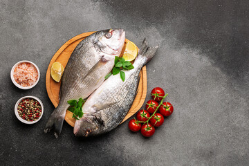 Raw dorado fish with spices, cherry tomatoes and Himalaya salt on the wooden plate on black stone...