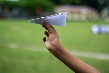 A man is holding a paper airplane with his hands and a blurred background