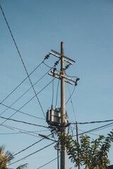 Power Pole with Transformer and Tangled Wires Against Clear Blue Sky