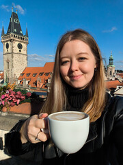 Tourist enjoying a cappuccino on a rooftop in prague with a view of the old town hall