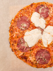 Baked frozen pizza with salami and burrata cheese baking on parchment paper