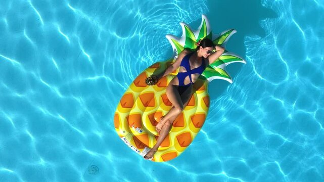 Beautiful woman in bikini relaxing on inflatable float in a pool at luxury resort, drone view. Concept summer beauty, sunbathing, relaxation and tropical vacation.