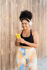 Happy plus size sportswoman using mobile phone app and wearing headphones after training outside