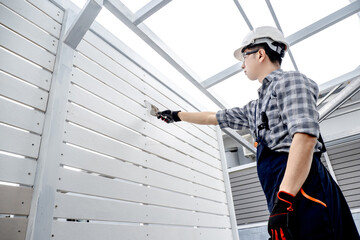 Asian male construction worker using plastering trowel for bolt head grouting on white wooden wall panel. Construction defect repair process
