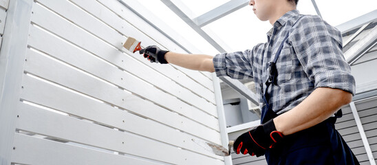 Construction worker man using paintbrush and plastering trowel for bolt head grouting on white wooden wall panel. Construction defect repair process
