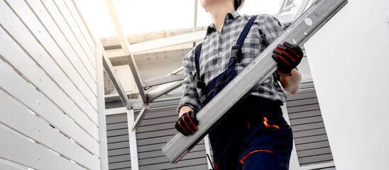 Male construction worker installing steel beam at building site. Roofer man carrying metal part of roof structure. Roof installation process. House extension and renovation concept