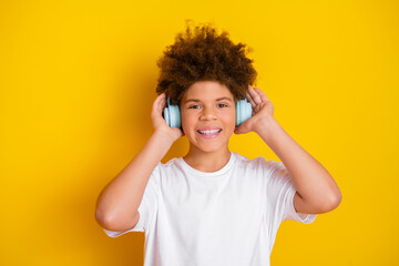 Smiling boy with afro hairstyle wearing headphones and white t-shirt on a vibrant yellow background