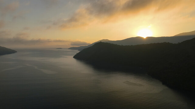 Aerial view of a serene sunrise casts golden light over the dark, rippling waters and silhouetted mountains, a tranquil vista from above., Rio de Janeiro, State of Rio de Janeiro, Brazil.