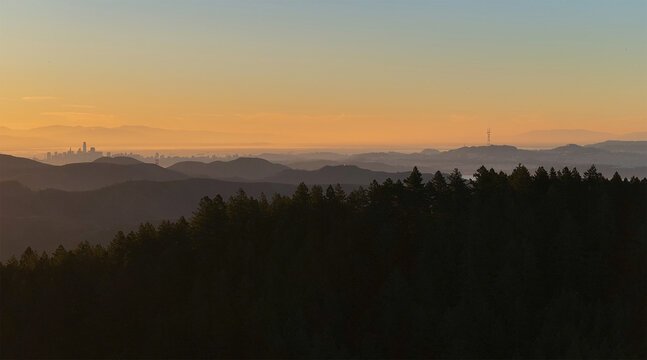 Aerial view of the silhouetted skyline of San Francisco rising through the morning mist, framed by dark forests and rolling hills under a gradient sky., San Francisco, California, United States.