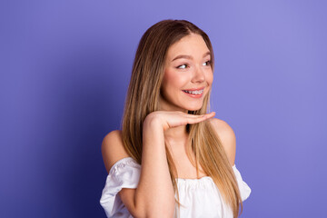 Smiling young woman with braces posing stylishly in casual white top on a vibrant purple background...