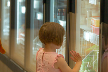 A little girl wearing a bright pink dress is curiously looking into an open refrigerator filled...