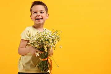 Smiling little boy with bouquet of beautiful chamomile flowers on yellow background. Space for text