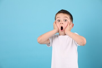 Portrait of surprised boy on light blue background, space for text