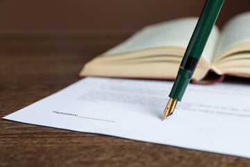 Signing notary document with fountain pen at wooden table against brown background, closeup