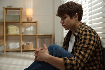 Teen problems. Depressed teenage boy near window at home, space for text