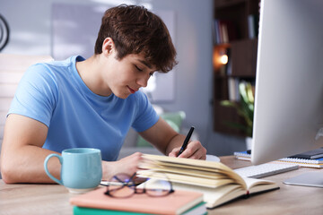 Teenage student taking notes while studying at table indoors