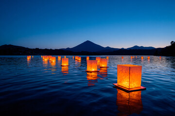paper lanterns floating over serene lake surface, mountain silhouettes in background