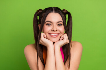 Bright young woman with trendy ponytails posing against a vibrant green background exuding...