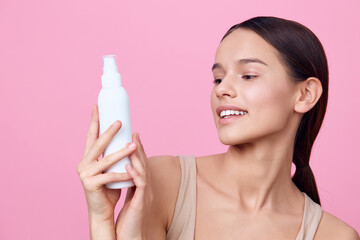 Young woman holding a skincare product against a pink background, showcasing healthy skin and a...