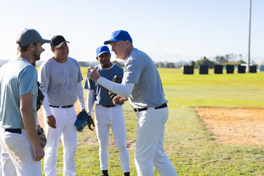 Diverse male baseball team standing and gesturing on baseball field with gloves near infield