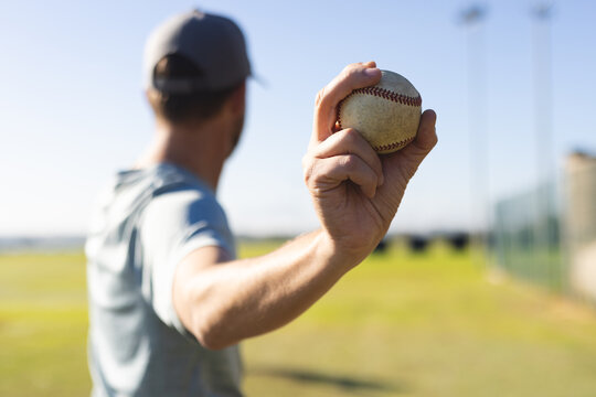 Man wearing t-shirt and baseball cap pitching baseball on baseball field near fence, copy space
