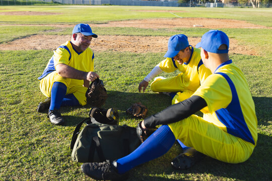 Male teammates sorting gloves and chatting in yellow blue jerseys on infield grass at ballpark