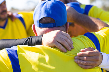 Senior male teammates huddling before game on baseball field wearing yellow jerseys and blue cap