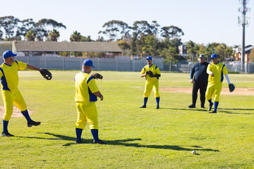 Male baseball team and coach standing on suburban field catching baseball with gloves and caps