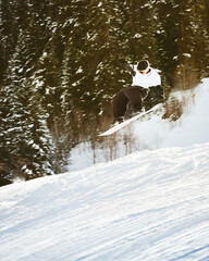 Young kid Snowboarder training in white jacket black pants jumps off freestyle on snowy slope...